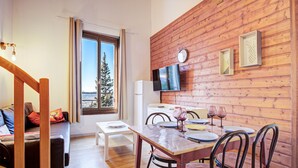 Ein gemütlicher Essbereich mit einer Holzwand, einem für zwei Personen gedeckten Esstisch und Blick auf einen Baum durch ein Fenster.