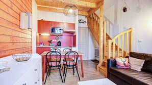 Ein gemütliches Interieur mit Holzbalkendecke, einer Essecke mit Stühlen und Tisch, einer Küche mit Mikrowelle und einer Treppe.