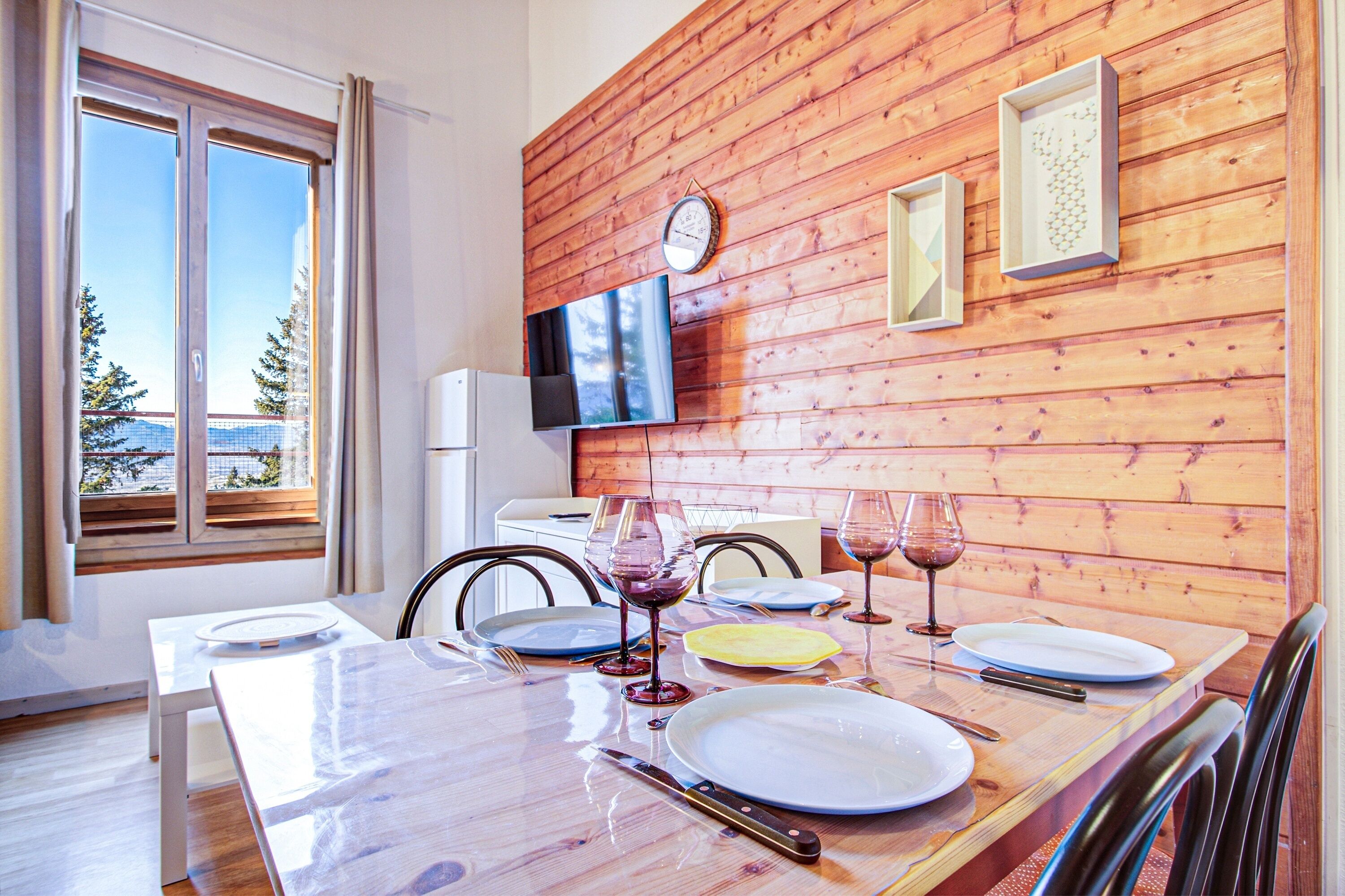 A dining area with a wooden wall, a clock, and framed artwork.