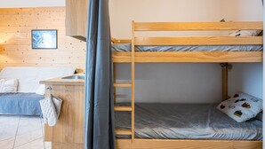 En køjeseng med trægavl, et lille skrivebord med håndvask og et vindue med udsigt til træer.