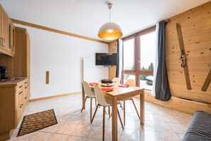 A dining area with a wooden table, chairs, and a television on the wall. - Le Cœur des Neiges - Station de ski à pied (Villarembert)