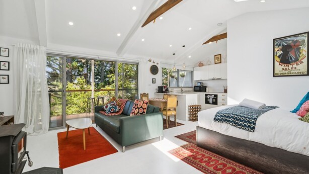 Ein moderner, offener Wohnbereich mit einer großen Schiebeglast ür, die auf einen Balkon führt, einer gemütlichen Sitzecke mit einer Couch und einem Esstisch sowie einem separaten Schlafzimmer mit einem Bett und einem großen Fenster.