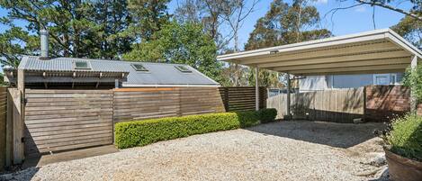 A residential property with a covered outdoor area, a fenced yard, and a gravel driveway.