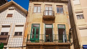 Um edifício com várias andares, fachada estampada, persianas verdes e varanda com grades de metal.