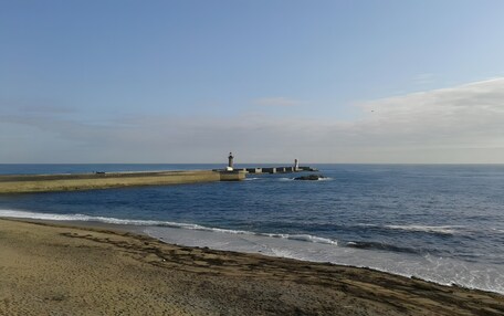A coastal scene with a lighthouse, a sandy beach, and calm sea.
