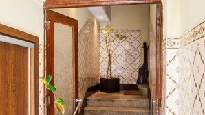 Uma escadaria com corrimão de madeira, um vaso de planta e azulejos decorativos na parede.
