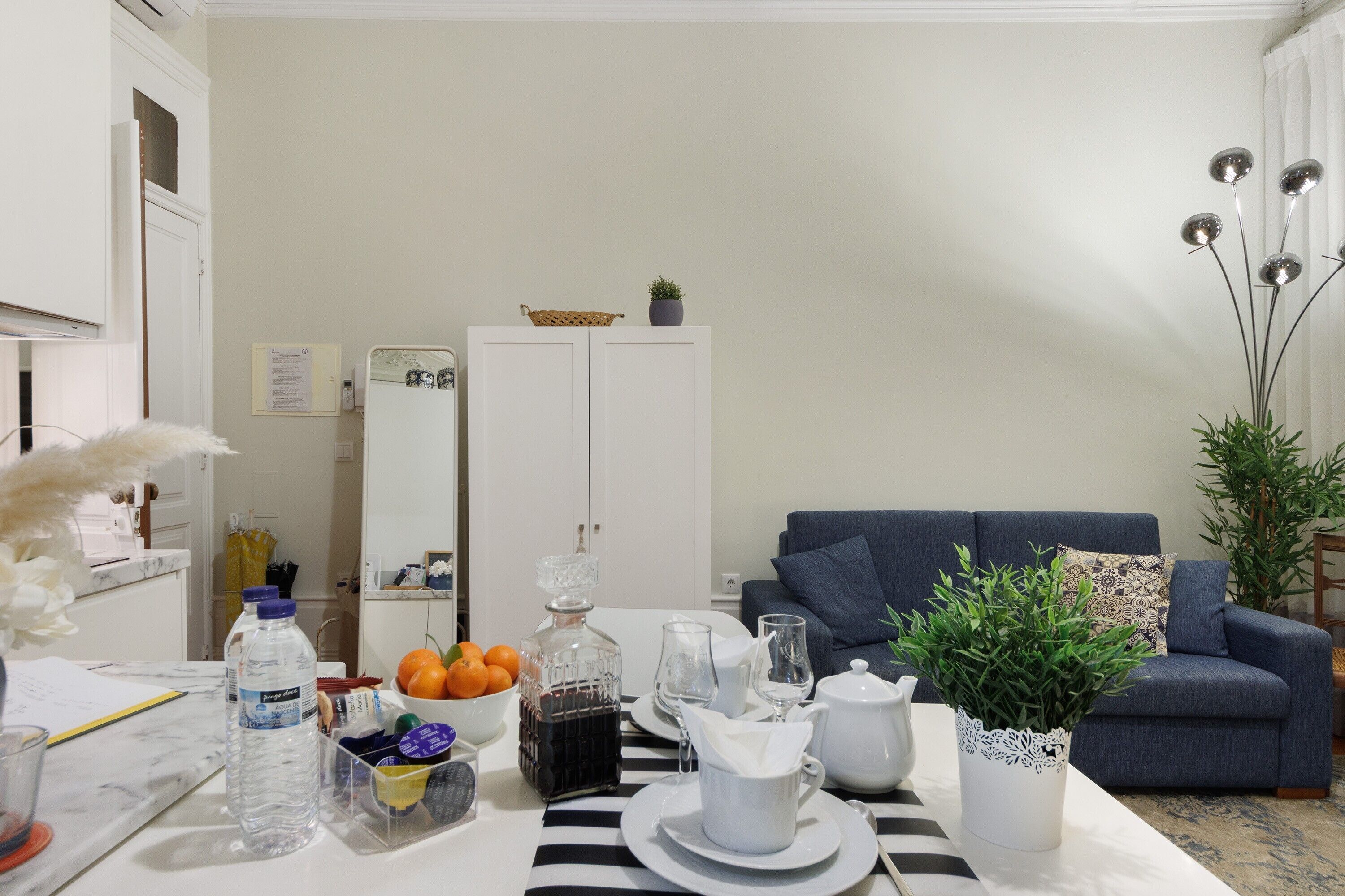 A dining area with a table set for two, a blue sofa, and a potted plant.