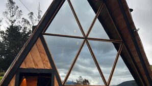 Eine dreieckige Holzhütte mit einem großen Panoramafenster und einer Holztreppe, die zu einer oberen Ebene führt.
