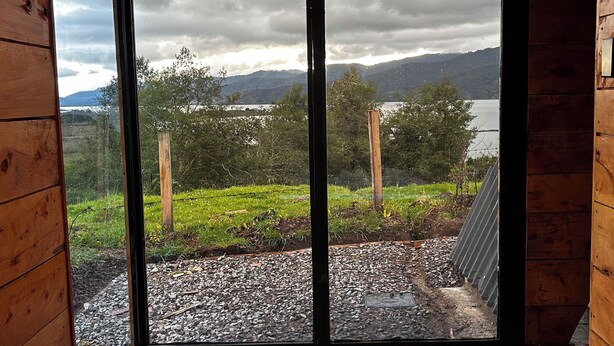 Ein Holzinnenraum mit einem großen Fenster, einer Badewanne und Blick auf einen See und Berge.
