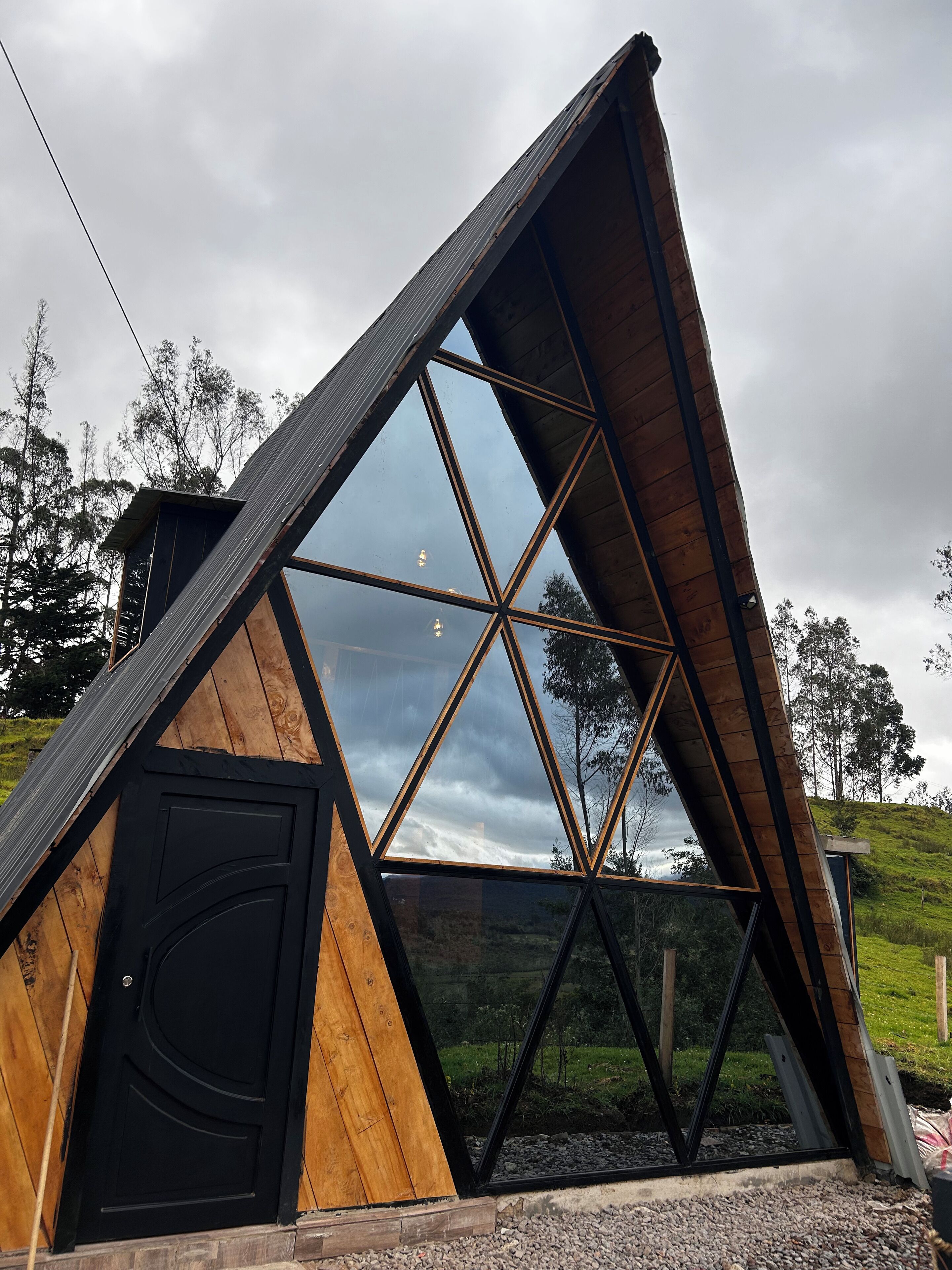 Eine dreieckige Holzhütte mit einer schwarzen Tür und großen Fenstern.