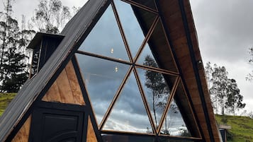 Eine dreieckige Holzhütte mit einer schwarzen Tür und großen Fenstern.