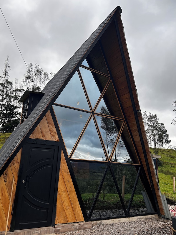 Una estructura de madera triangular con una puerta negra y ventanas amplias.