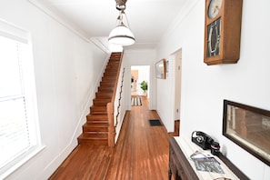 A wooden staircase leading to a landing with a hanging light fixture, a wall-mounted clock, and a telephone. - The Sago Palm House (Thomasville)