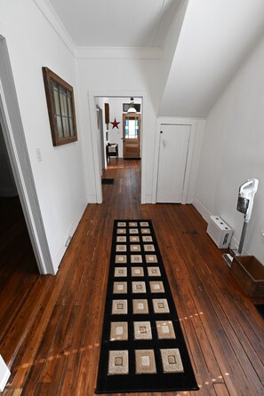 A hallway with wooden flooring, a black and beige rug, a white door, and a ceiling fan. - The Sago Palm House (Thomasville)