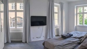 Ein Schlafzimmer mit einem Bett, einem an der Wand befestigten Flachbildfernseher und einem Fenster mit Vorhängen.