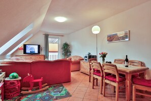 Ein gemütliches Wohnzimmer mit einem roten Sofa, einem Fernseher, einem Esstisch mit Stühlen und einem Deckenventilator.