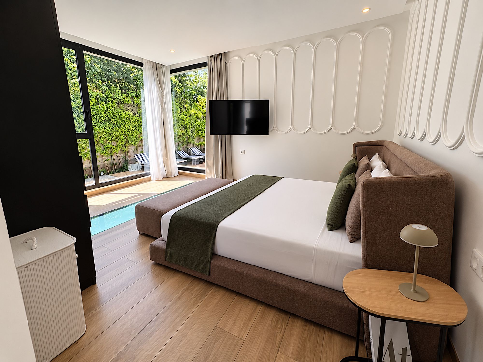 Une chambre moderne avec un grand lit, une télévision, une table de chevet et une vue sur une piscine.