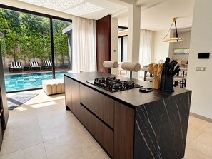 A modern kitchen with a marble island, a dining area with a pool view, and a living space with a large window overlooking greenery. - Palais Zahira (Marrakech)