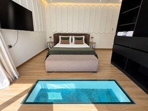 Ein modernes Schlafzimmer mit Bett, Nachttischen, einem integrierten Fernseher, einer Glasbodenplatte und einem schwarzen Stauraumelement.