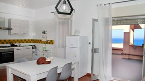Une cuisine compacte avec un coin repas, un réfrigérateur et une vue sur la mer depuis un balcon.