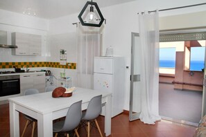 Eine kompakte Küche mit Essbereich, einem Kühlschrank und Meerblick vom Balkon.