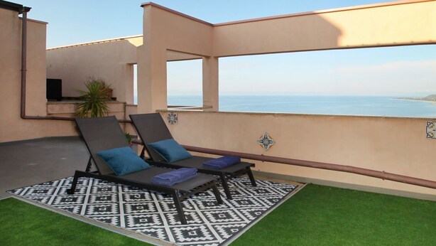 Une terrasse sur le toit avec deux chaises longues, un tapis à motifs et une vue sur la mer.