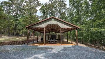 Ein überdachter Pavillon mit Picknicktisch und Grill, umgeben von bewaldeter Landschaft.