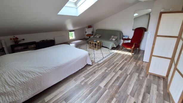 A bedroom with a large bed, a sofa, a red chair, a small table, and a skylight. - o\tSelf-contained studio in house 3 km from Annecy town center, (Seynod)