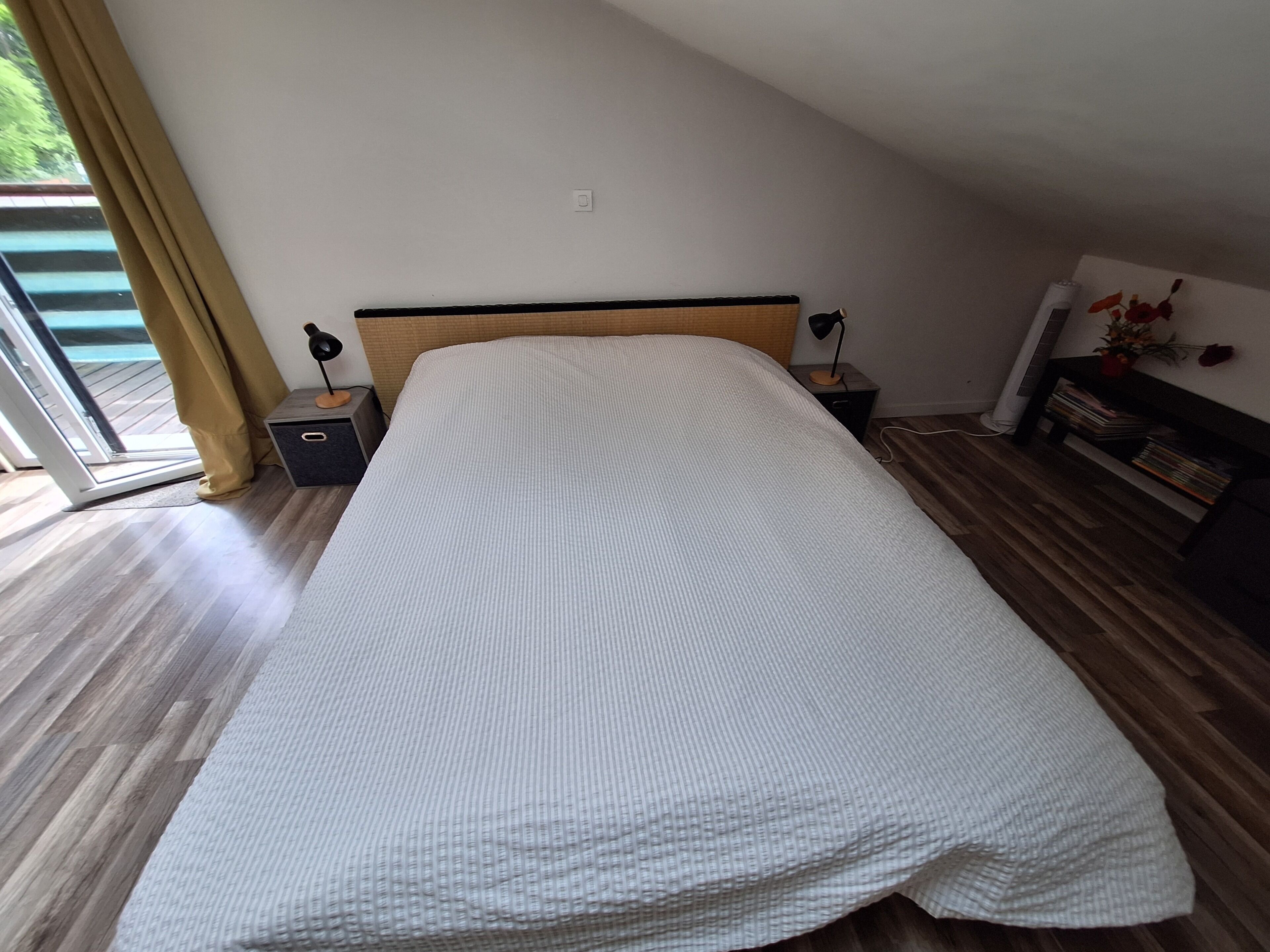 Une chambre à coucher comprenant un lit, des tables de chevet, une lampe, une petite table, une bibliothèque et une porte-fenêtre coulissante.