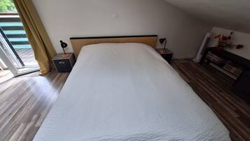 Une chambre à coucher comprenant un lit, des tables de chevet, une lampe, une petite table, une bibliothèque et une porte-fenêtre coulissante.