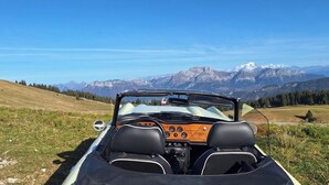 A convertible car parked on a grassy hill with a mountainous landscape in the background. - o\tSelf-contained studio in house 3 km from Annecy town center, (Seynod)