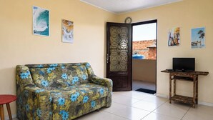 A living room with a floral sofa, a TV on a wooden stand, and a balcony door. - Casa a 900m da Praia do Pontal em Cabo Frio (Cabo Frio)