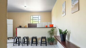 A compact kitchen with a window, a refrigerator, a sink, and a countertop with stools and potted plants. - Casa a 900m da Praia do Pontal em Cabo Frio (Cabo Frio)