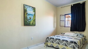 A bedroom with a bed, a window with curtains, and a painting on the wall. - Casa a 900m da Praia do Pontal em Cabo Frio (Cabo Frio)