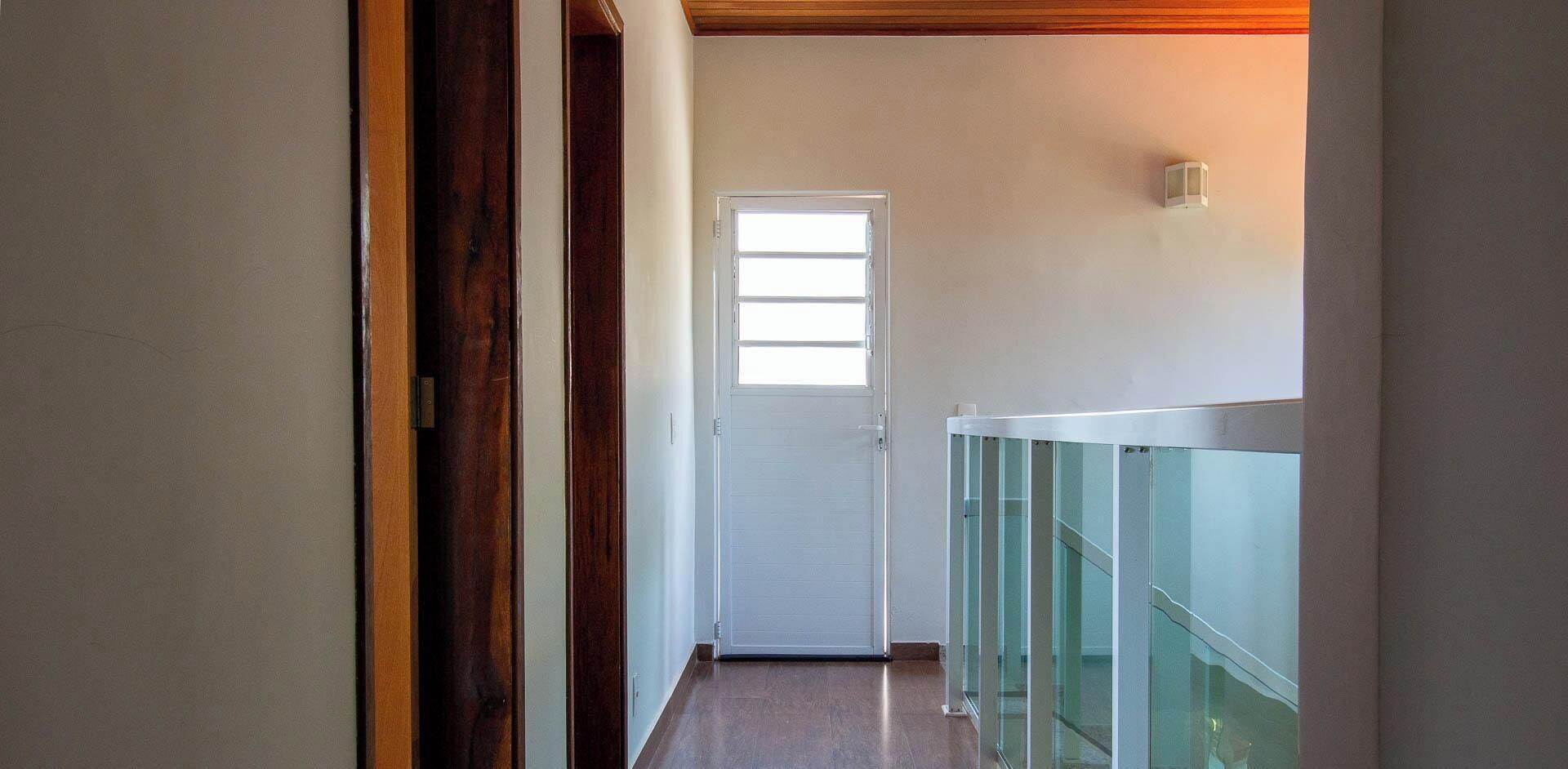 Un corridoio con una porta in legno, una porta bianca in fondo e una ringhiera in vetro sulla destra.