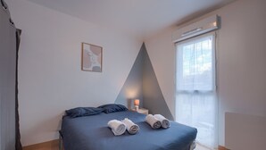 A modern bedroom with a large bed, a bedside table with a lamp, a framed picture on the wall, and a window with blinds. - La Grange - Proche Centre & Parking (Laval)