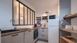 A compact kitchen with a sink, stove, microwave, and wooden shelves. - La Grange - Proche Centre & Parking (Laval)