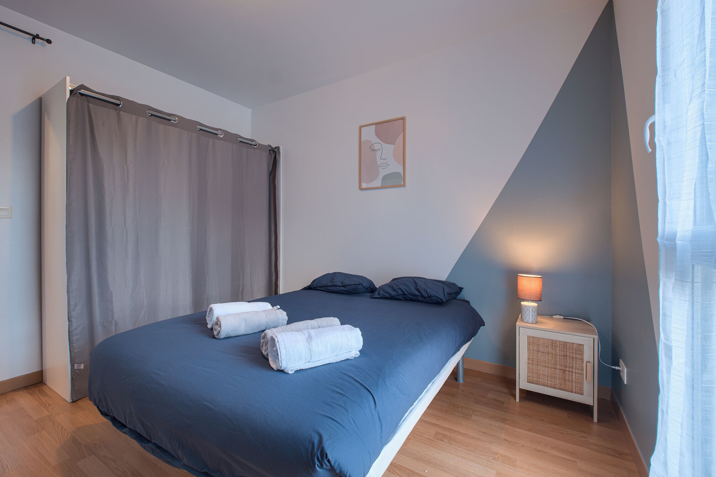 A bedroom with a bed, a nightstand, a lamp, and a wall-mounted artwork.