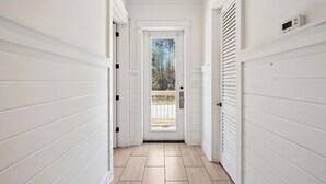 A narrow hallway with white walls and a wooden floor, leading to a door with a view of trees outside. - Pelican Perch (Seagrove Beach)