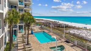 A pool area with a view of the beach, lounge chairs, and a building with balconies. - Seabreeze (101B) (Destin)