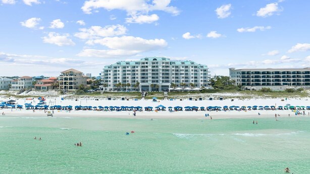 A beachfront hotel with multiple floors, a sandy beach in front, and several umbrellas. - Seabreeze (101B) (Destin)