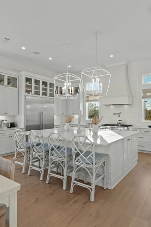 Une cuisine spacieuse avec des meubles blancs, un grand îlot central doté de tabourets et un éclairage suspendu.