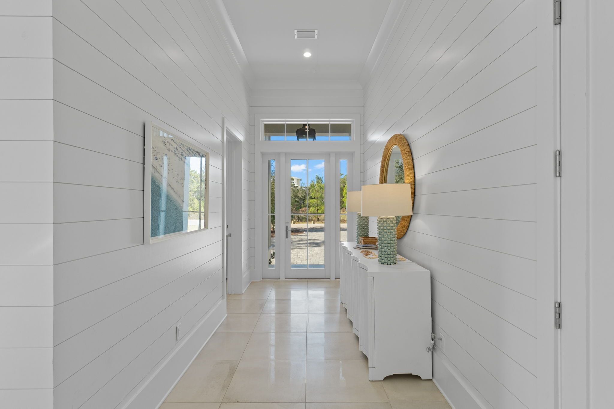 A hallway with white paneling, a large mirror, and a door leading to a patio.