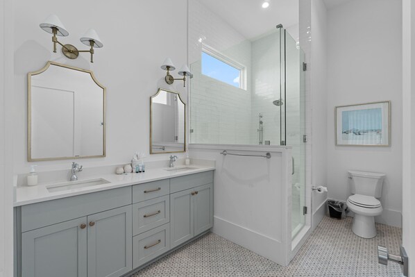 Une salle de bain moderne avec deux lavabos, un grand miroir, une cabine de douche et des toilettes.