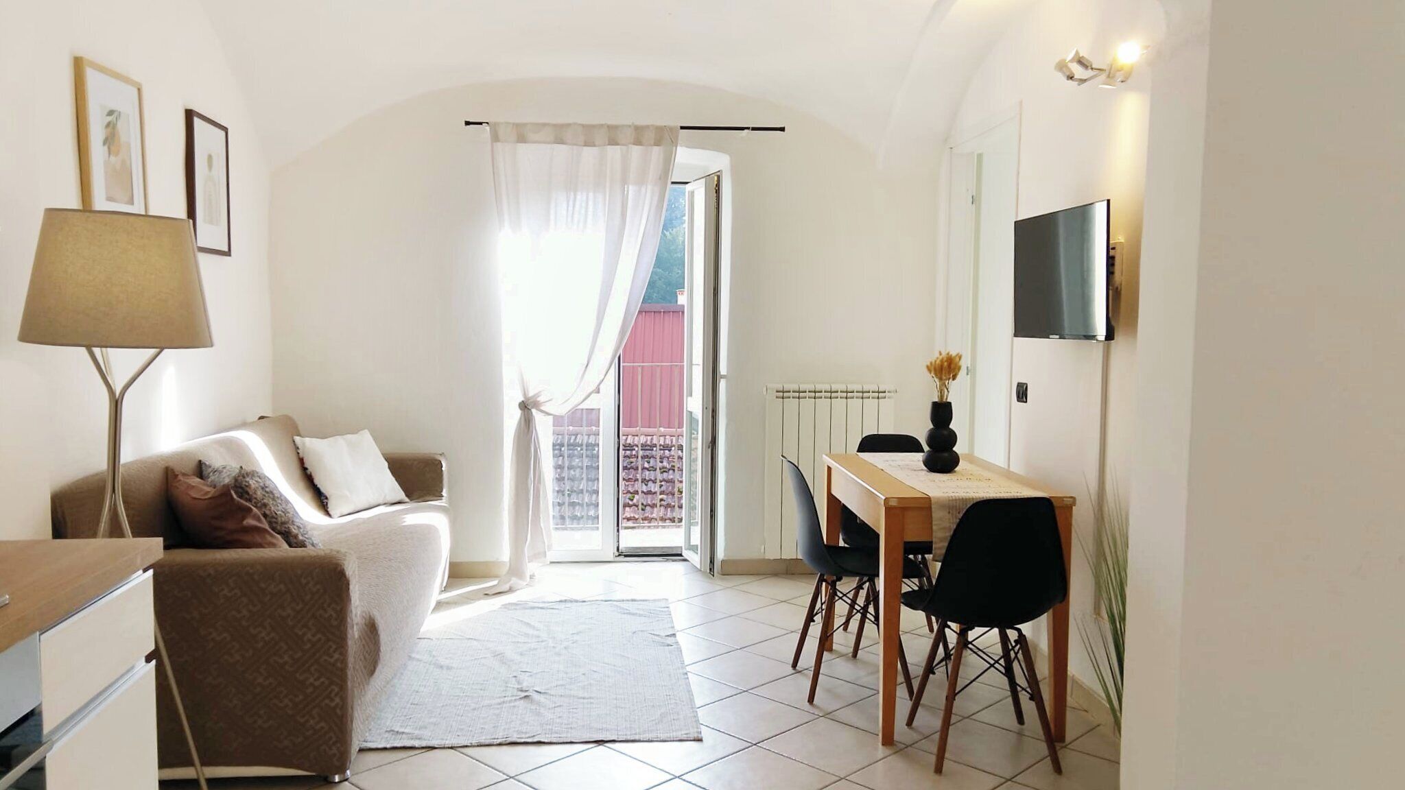 Un espace de vie compact comprenant un canapé, une table à manger avec des chaises, un téléviseur fixé au mur et une vue sur un espace extérieur, accessible par une porte.