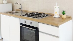 Een moderne keuken met witte kastjes, een roestvrijstalen afzuigkap, een gasfornuis, een inbouwoven en een kleine potplant.