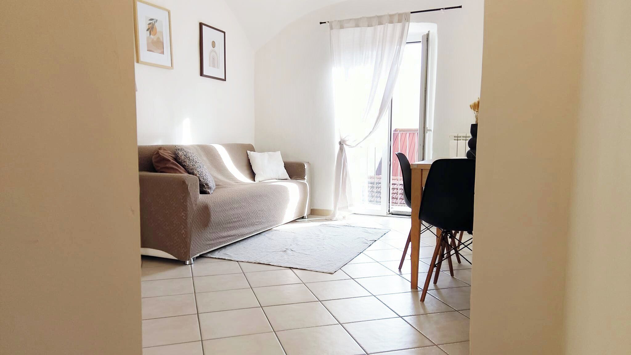 Een woonkamer met een beige bank, een wit tapijt en een eethoek met een tafel en stoelen.