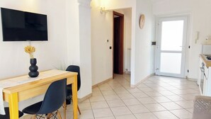 Een eethoek met een houten tafel en stoelen, een flatscreen televisie aan de muur en een deur naar een andere kamer.