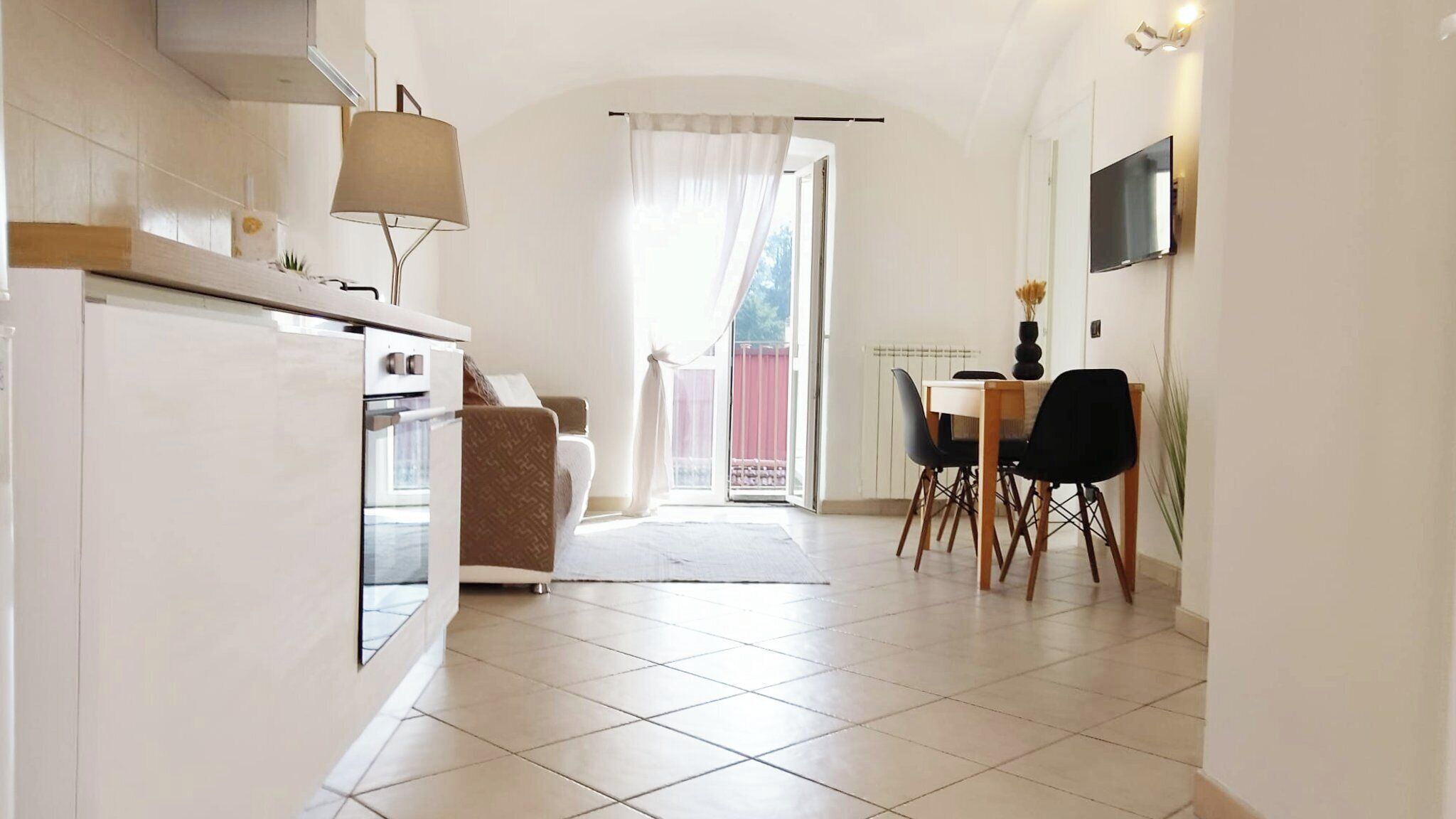 Une cuisine compacte comprenant un coin repas, un canapé et un téléviseur fixé au mur.