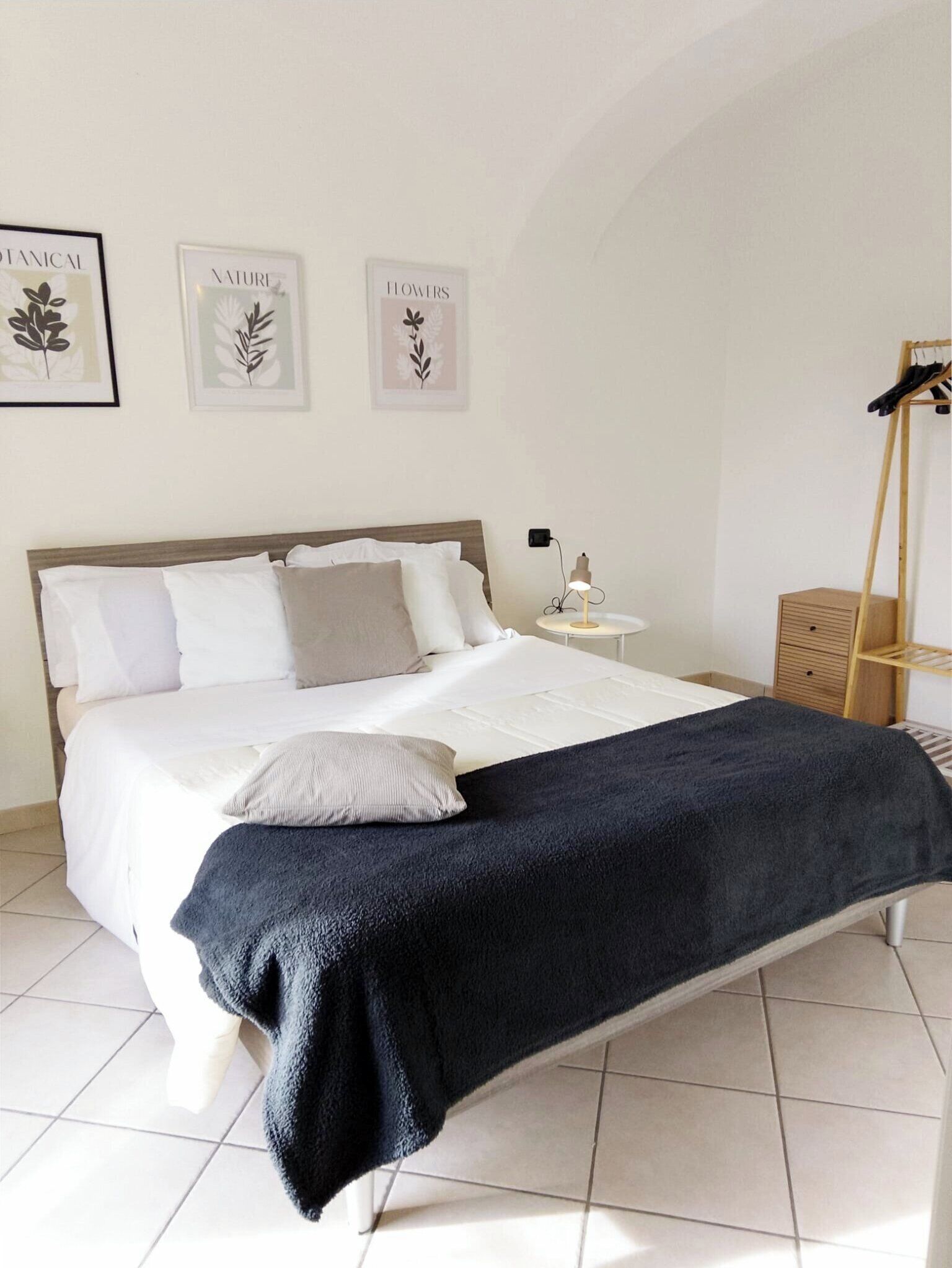 A neatly made bed with white and grey bedding, a dark blue throw blanket, and a small bedside table with a lamp.